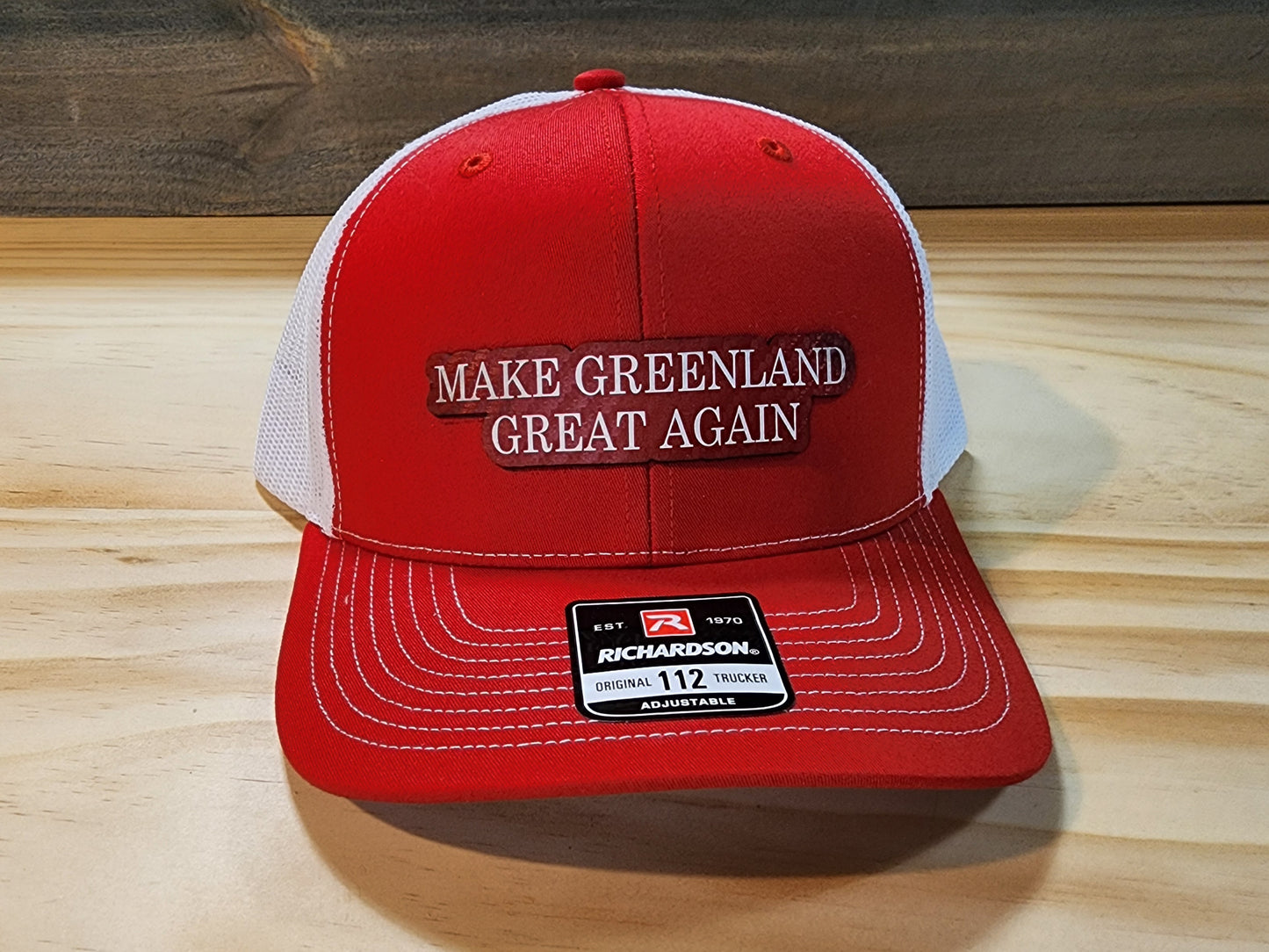 Three "Make Greenland Great Again" hats in red displayed on a wooden surface.