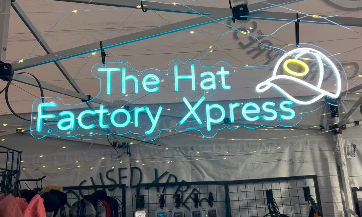 The Hat Factory Xpress neon sign glowing teal under the hat bar canopy