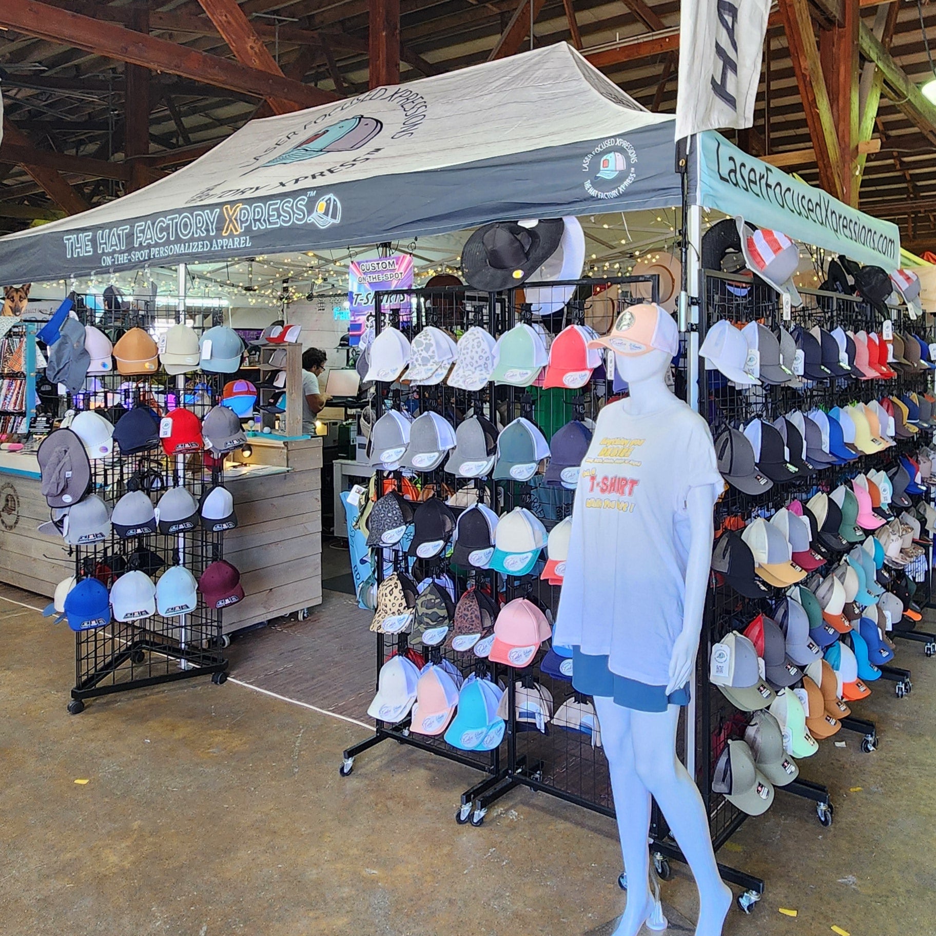 Indoor market or fair with people browsing stalls, including a hat display.