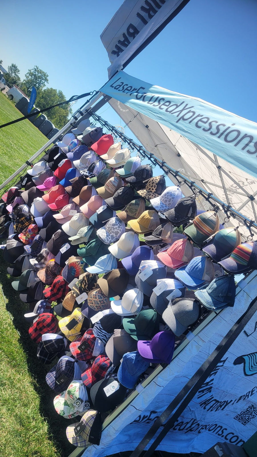 The cap wall at The Hat Factory Xpress® hat bar — rows of trucker and snapback caps in plaid, camo, denim, floral and solid colorways, hanging ready for guests to pick from