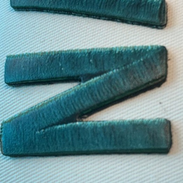 A letter-cut patch: a single teal letter N, cut to the shape of the letter itself
